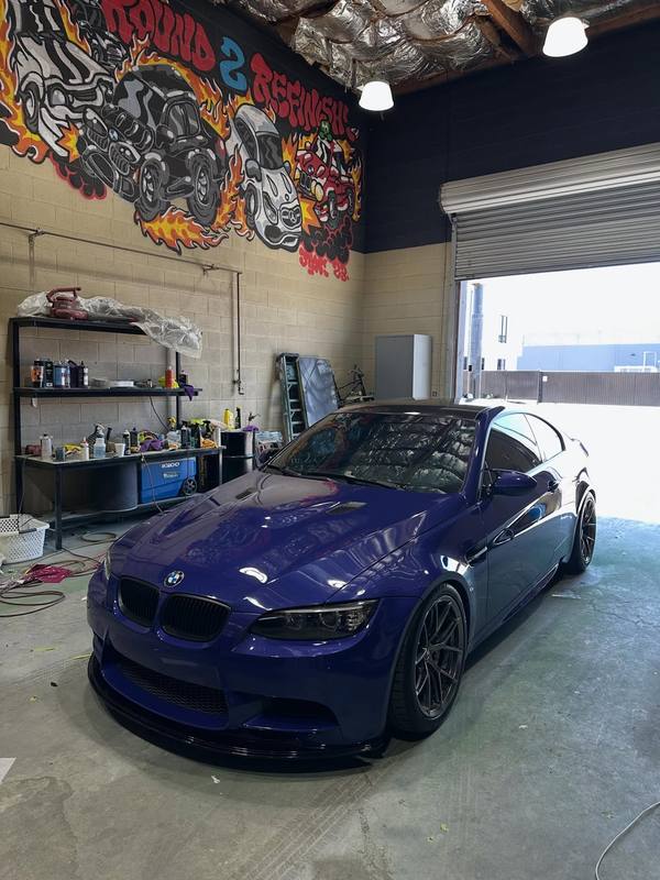 BMW E92 M3 after a Peel Clear color change to deep purple, the hood, bumper, fenders and mirrors all carrying the new color with enough gloss to mirror the open roll-up door, and the roof left black