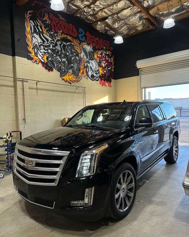 Cadillac Escalade ESV in gloss black inside the shop, the flame mural reflected across the hood and front door, with the chrome grille, window trim and running boards left bright against it