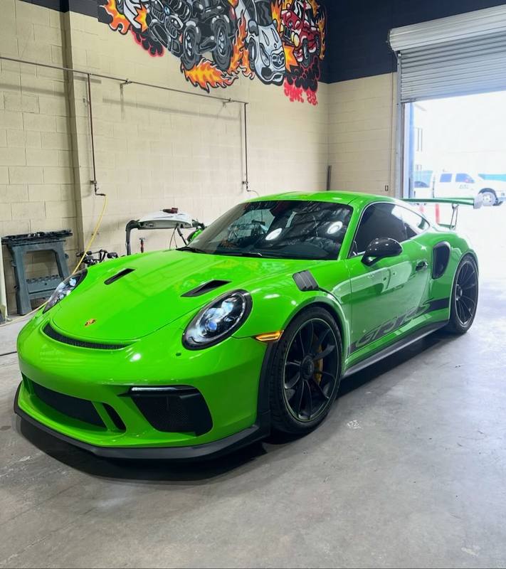 Porsche 911 GT3 RS in bright green in front of the flame mural, the gloss green running unbroken over the hood vents, the front lip and the louvres cut into the fenders