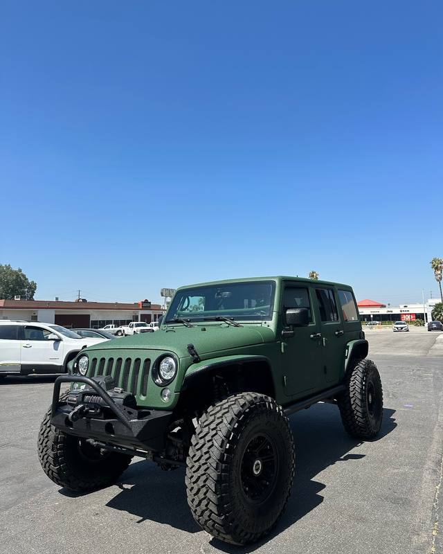 Lifted Jeep Wrangler in a textured matte army green that carries across the hood, hardtop, doors and fender flares in one tone; black steel front bumper with a winch, black wheels and mud tires