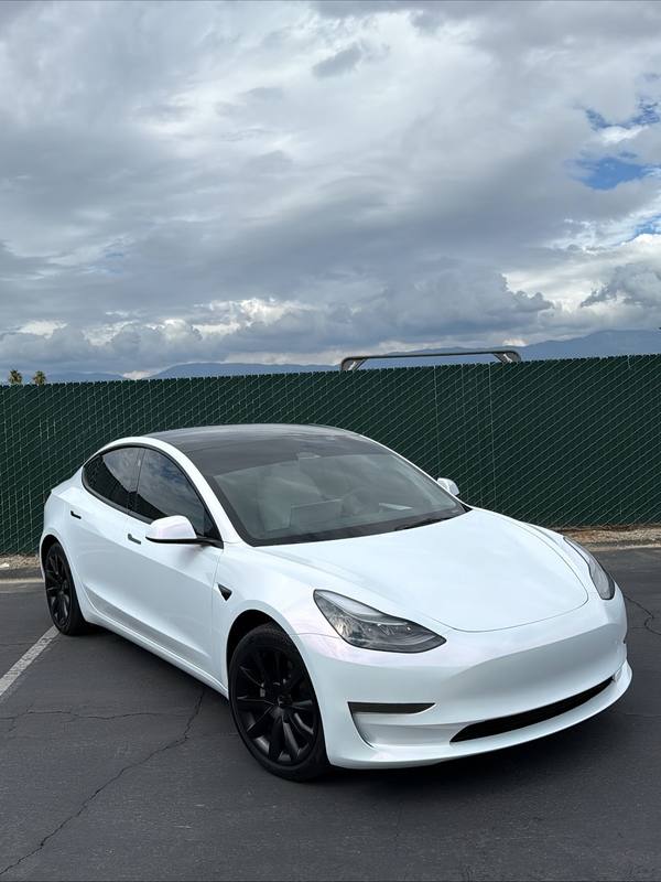 Pearl white Tesla Model 3 with satin black wheels, mirror caps and window surrounds and no bright trim anywhere on the car, the white flank holding a soft even reflection under a broken sky