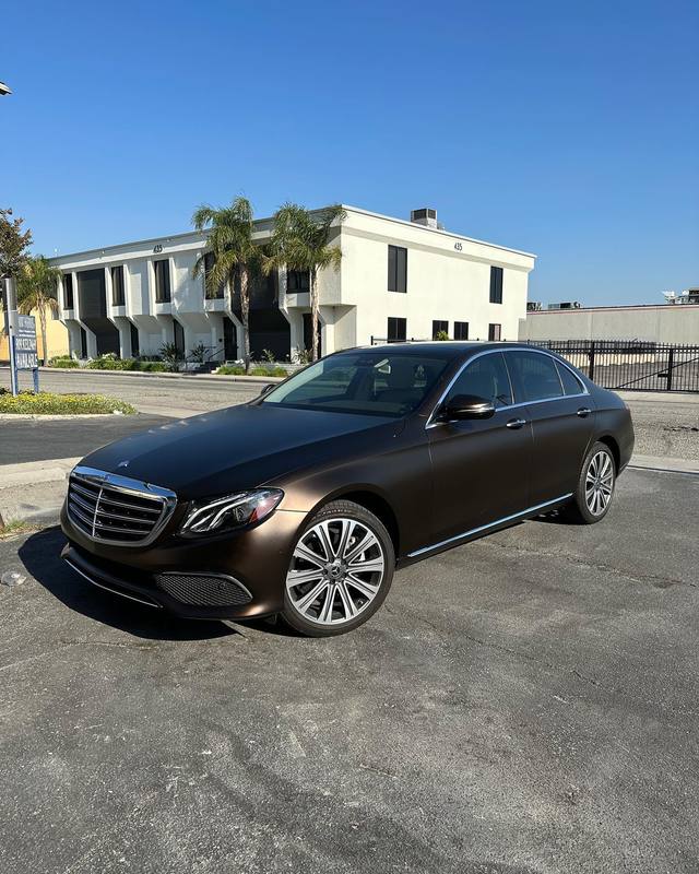 Mercedes-Benz E-Class in satin brown, hood, roof and doors all flat brown with the chrome grille, window surrounds and silver wheels left bright against it, parked in the lot outside Round 2 Refinish