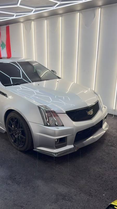 Cadillac CTS-V with its sunroof tinted, parked under the hexagon LED array, the array reflecting as clean hexagons across the silver hood and the glass above reading dark and even