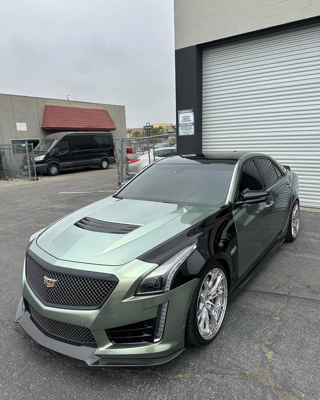 Cadillac CTS-V in two-tone sage green and gloss black, the split running hard down the fender and door with the hood, nose and front fenders green and the roof, rear doors and quarters black