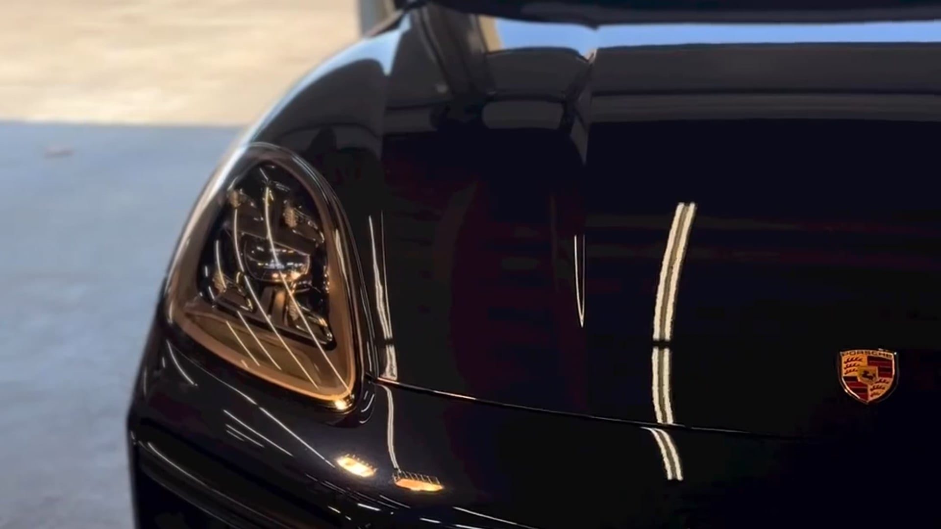 Close-up of a black Porsche front end, the hood and fender carrying one unbroken reflection line straight across the panel gap and the headlight lens clear enough to show the projector inside